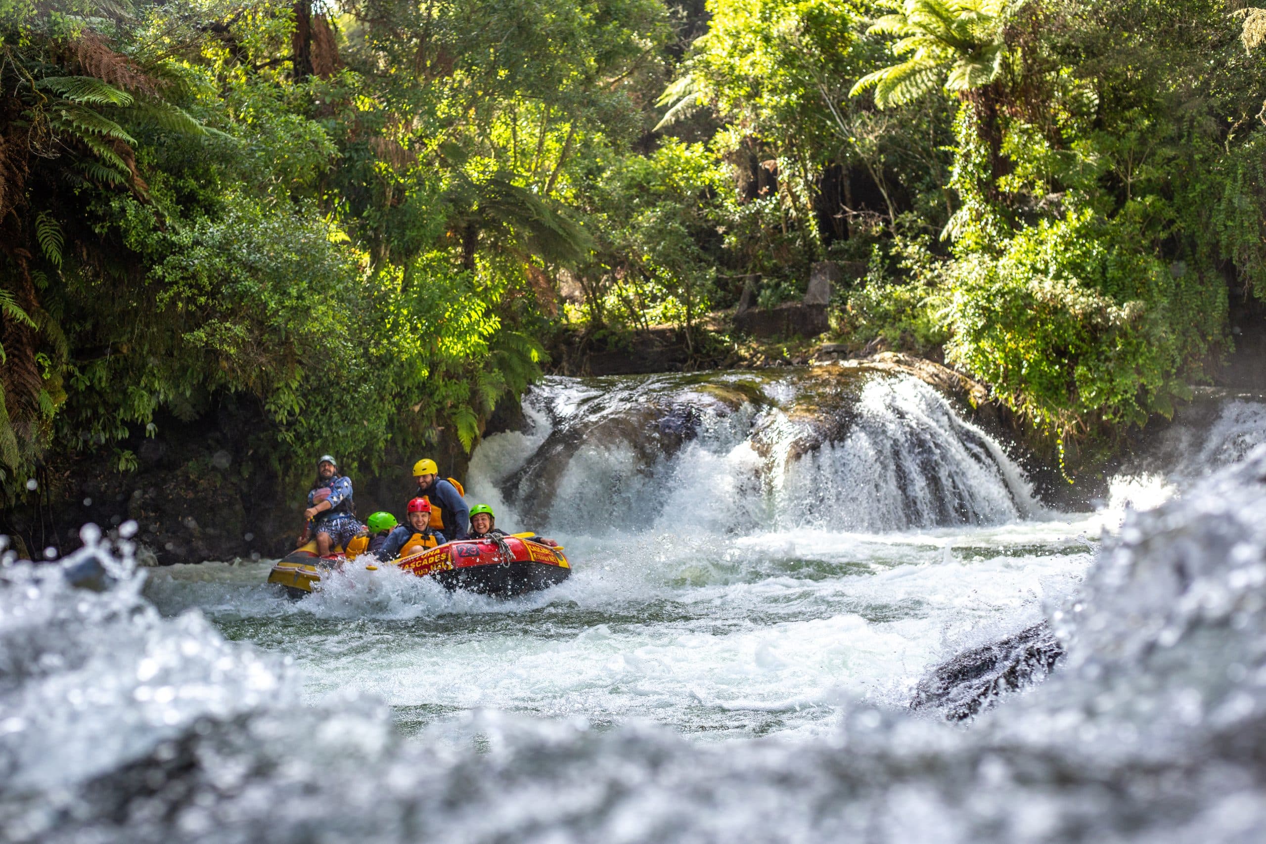 Group in a yellow raft paddling over a small waterfall surrounded by lush greenery.