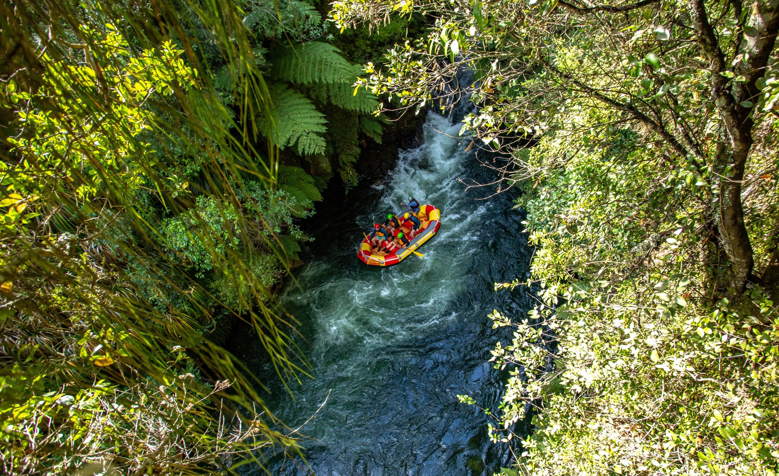 Rafters in a yellow raft descending a sloped waterfall with others following behind.