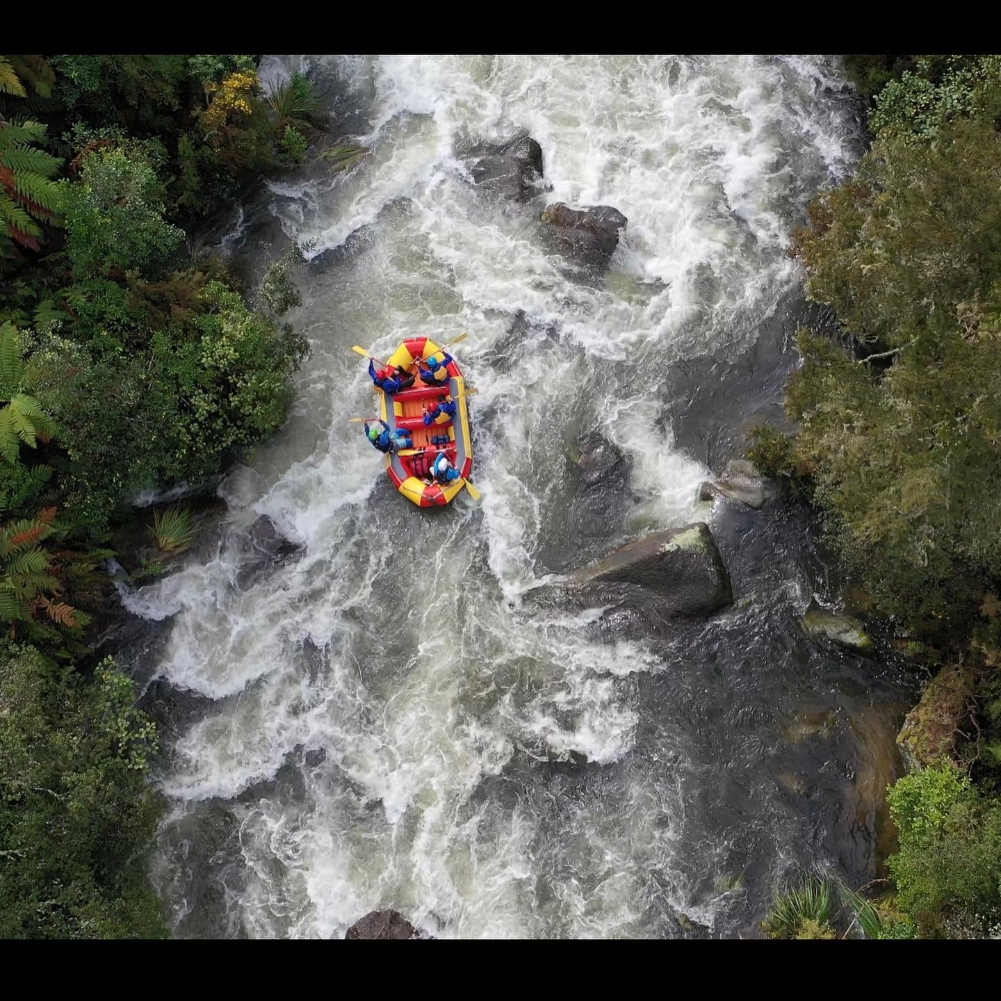 Rafters in a yellow raft descending a sloped waterfall with others following behind.