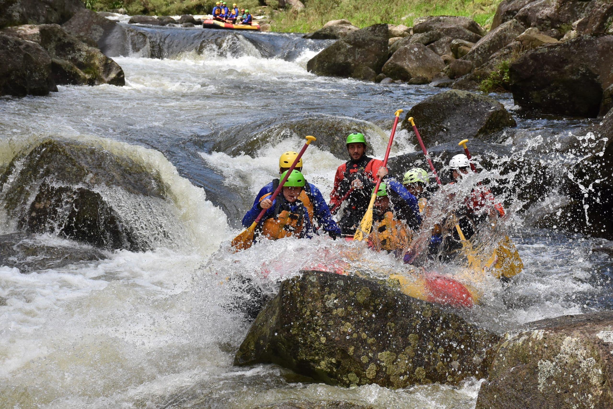 Rafters in a yellow raft paddling calmly down a green river under sunlight.